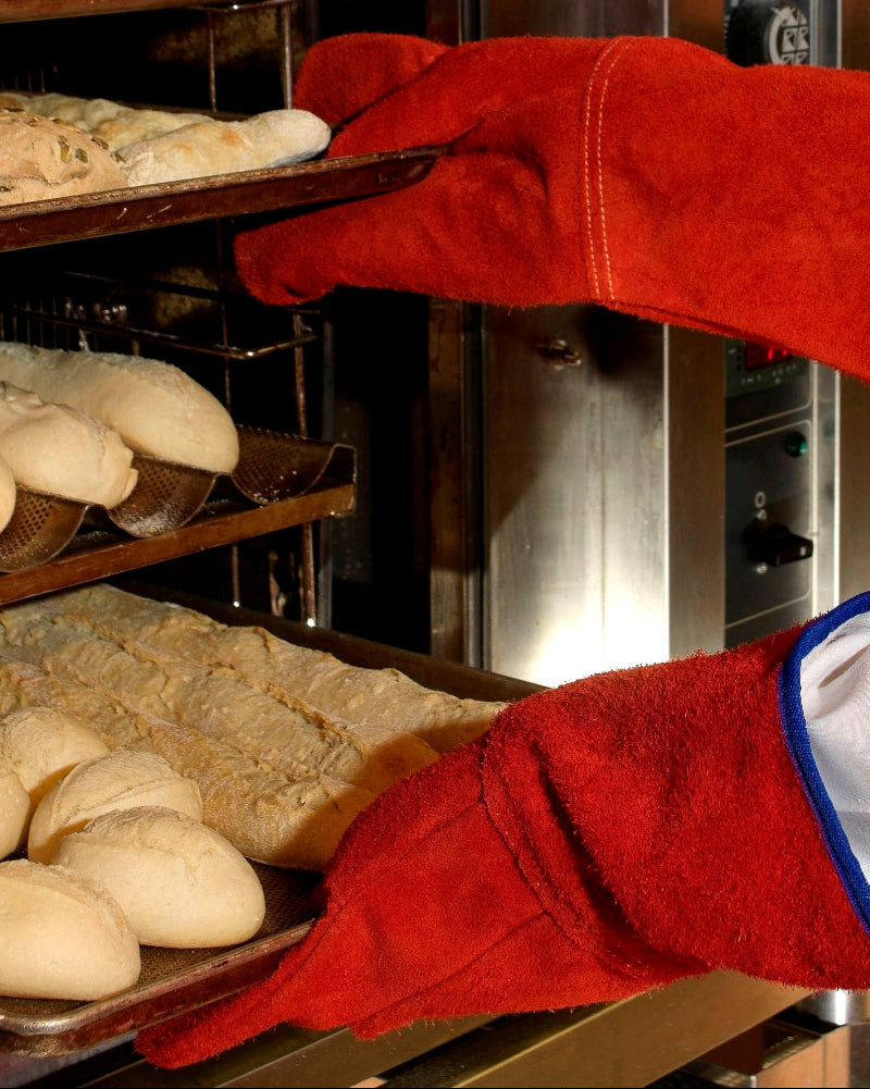 Guanti resistenti al calore Hotworks utilizzati in cucina per estrarre teglie di pane da forno industriale.
